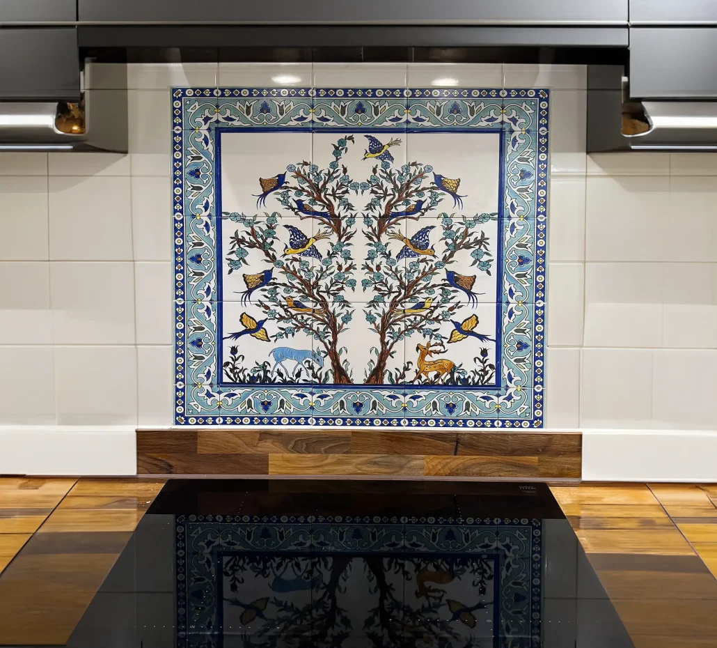 Tree of life tile mural framed by a decorative border on a backsplash above a kitchen cooktop