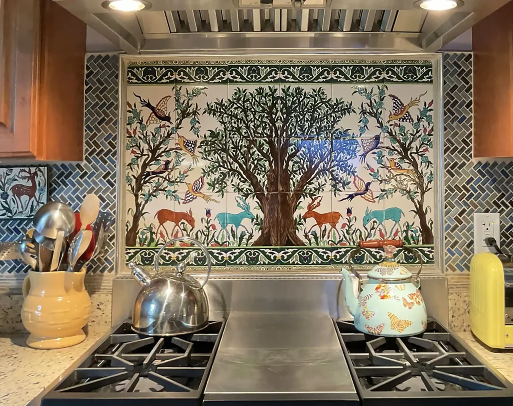 Olive tree tile mural framed by patterned field tiles above a kitchen range, an example of hand-painted backsplash cost