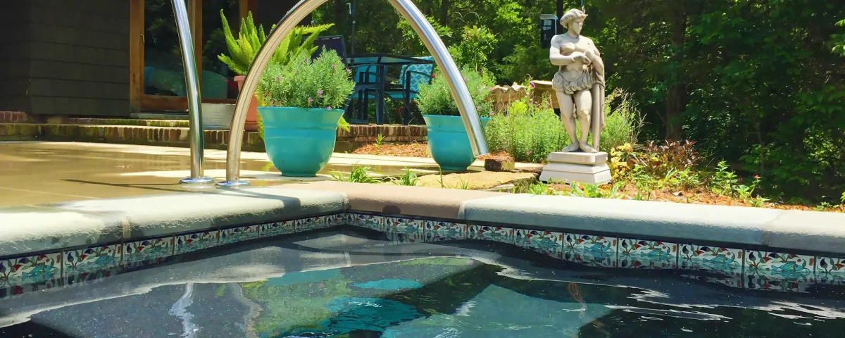 Patterned Balian waterline tiles beside submerged pool entry steps and a curved metal handrail