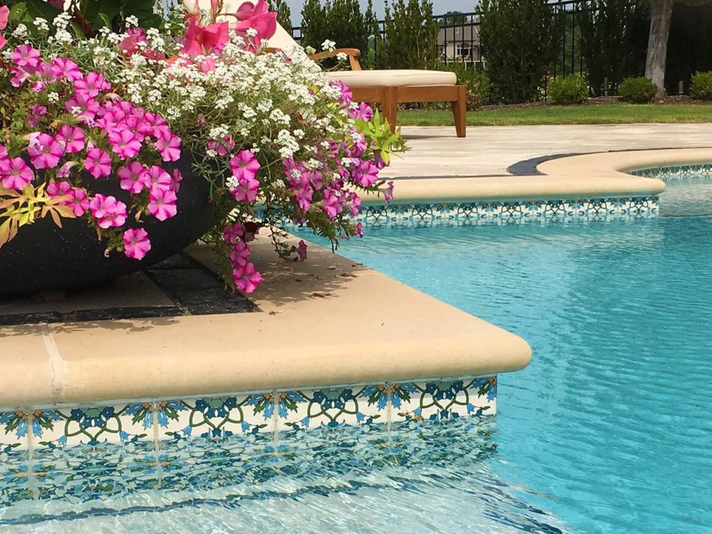 A row of porcelain pool tiles at the edge of a pool under a floral flowerpot