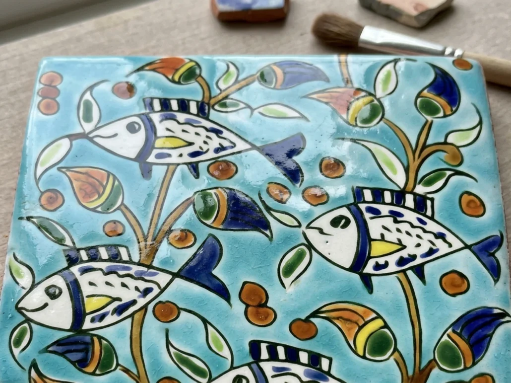 Hand painted tile on a table with painting brushes on top