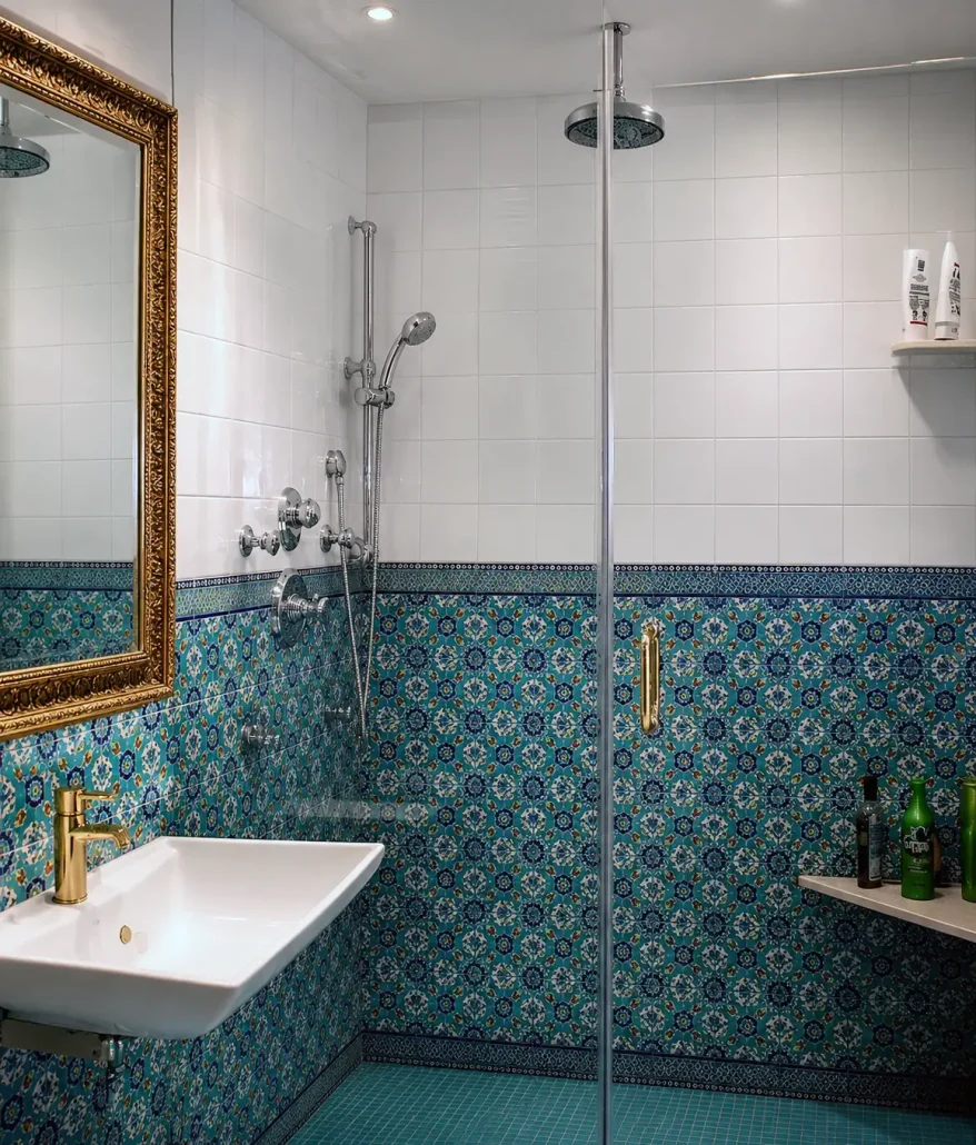 Modern bathroom shower with hand-painted blue and teal geometric patterned ceramic tiles, gold mirror and fixtures