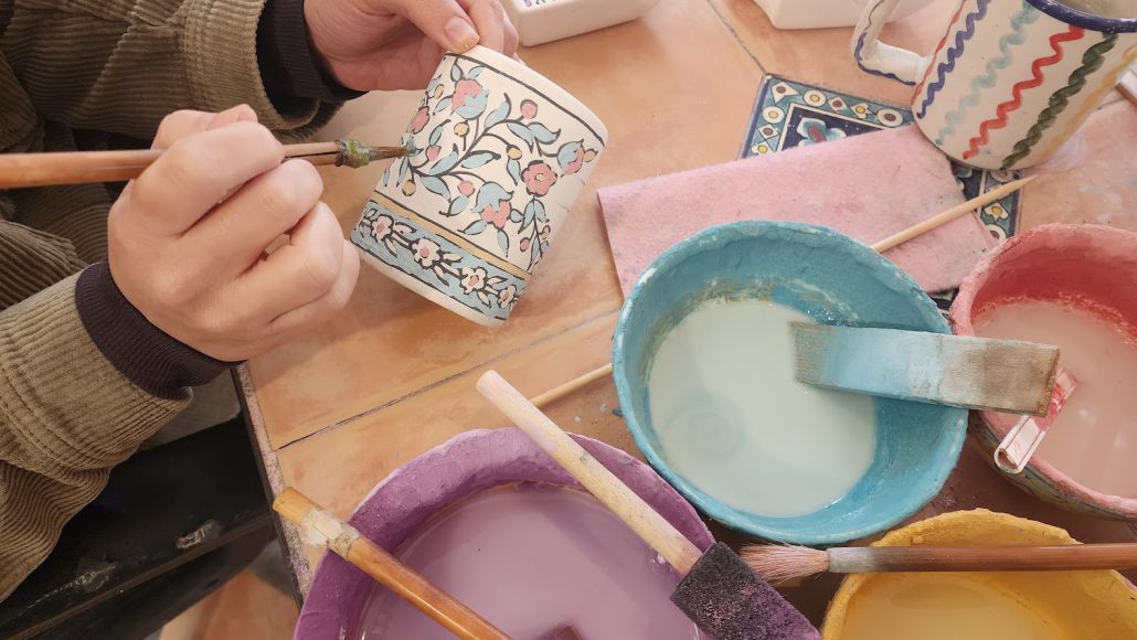 Balian artisan hand-painting floral motifs onto a ceramic mug using traditional ceramic glazes and brushes