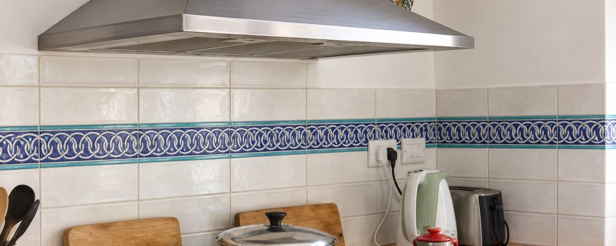 Blue and turquoise chain-pattern ceramic border across a cream tile backsplash behind a stainless steel range.