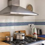 Blue and turquoise chain-pattern ceramic border across a cream tile backsplash behind a stainless steel range.