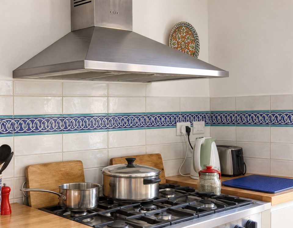 Blue and turquoise chain-pattern ceramic border across a cream tile backsplash behind a stainless steel range.