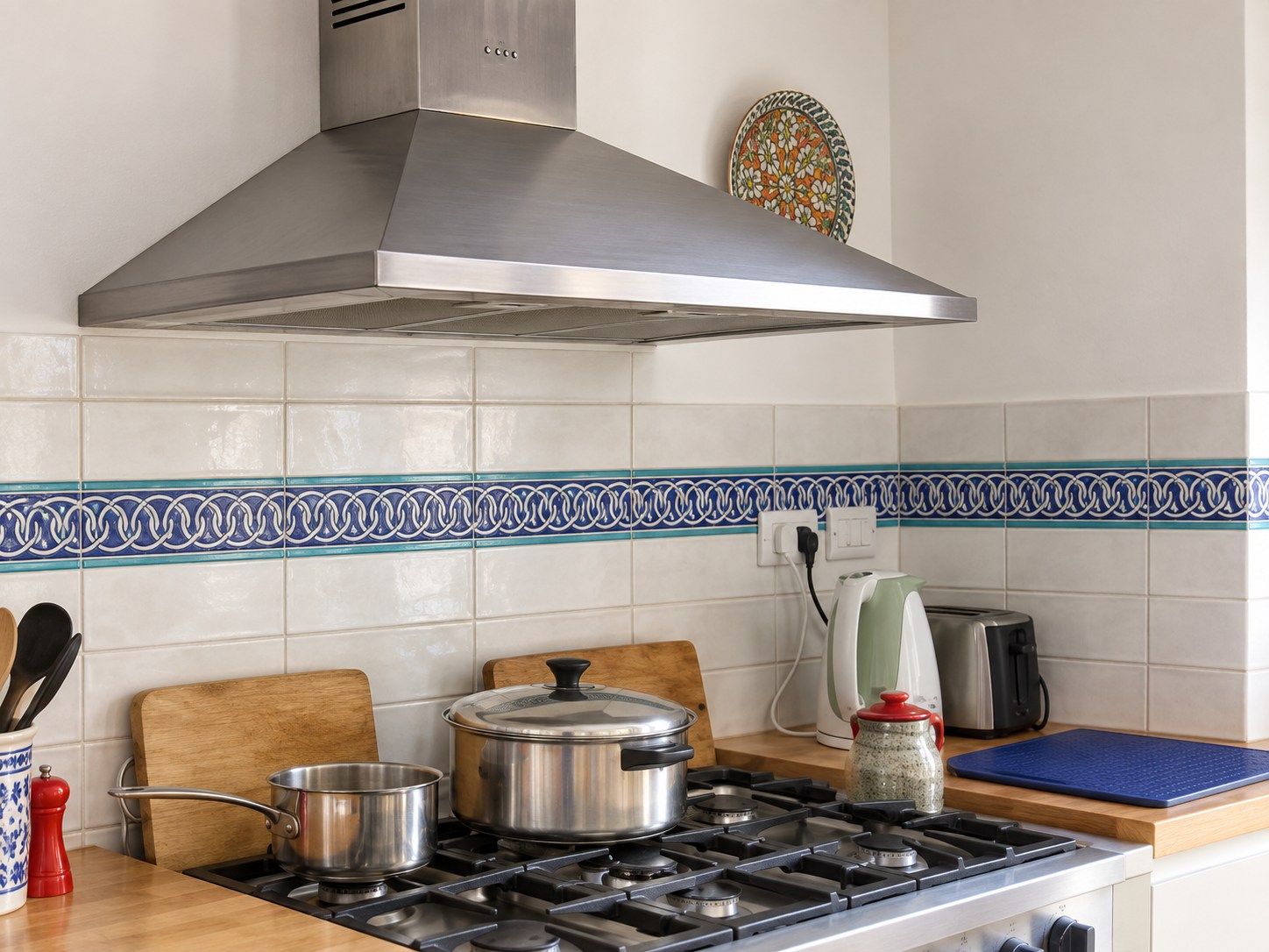 Blue and turquoise chain-pattern ceramic border across a cream tile backsplash behind a stainless steel range.